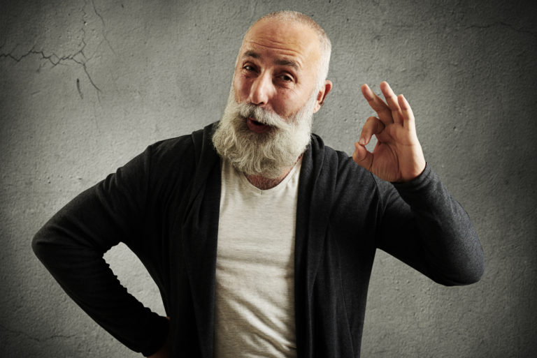 bearded senior man showing ok sign and looking at camera over grey wall